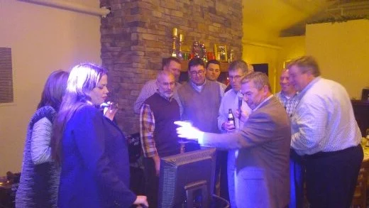 Coworkers gathered around the karaoke screen singing together at a corporate party