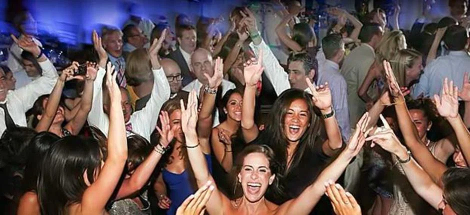A packed dance floor of wedding guests cheering with their hands in the air