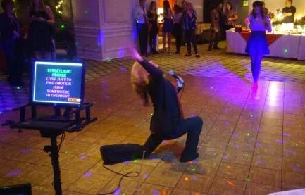 A guest performs karaoke on a lit dance floor in front of a lyrics screen