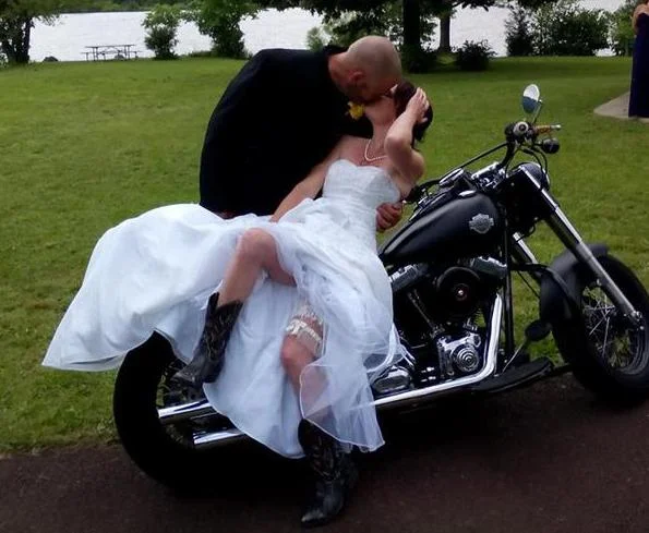 Groom and bride in her gown posing on a motorcycle