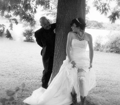 Black and white photo of a bride and groom playing around a tree