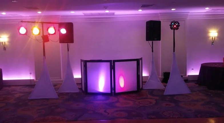 Deluxe wedding DJ setup with white facade, uplighting, and moving lights in a ballroom
